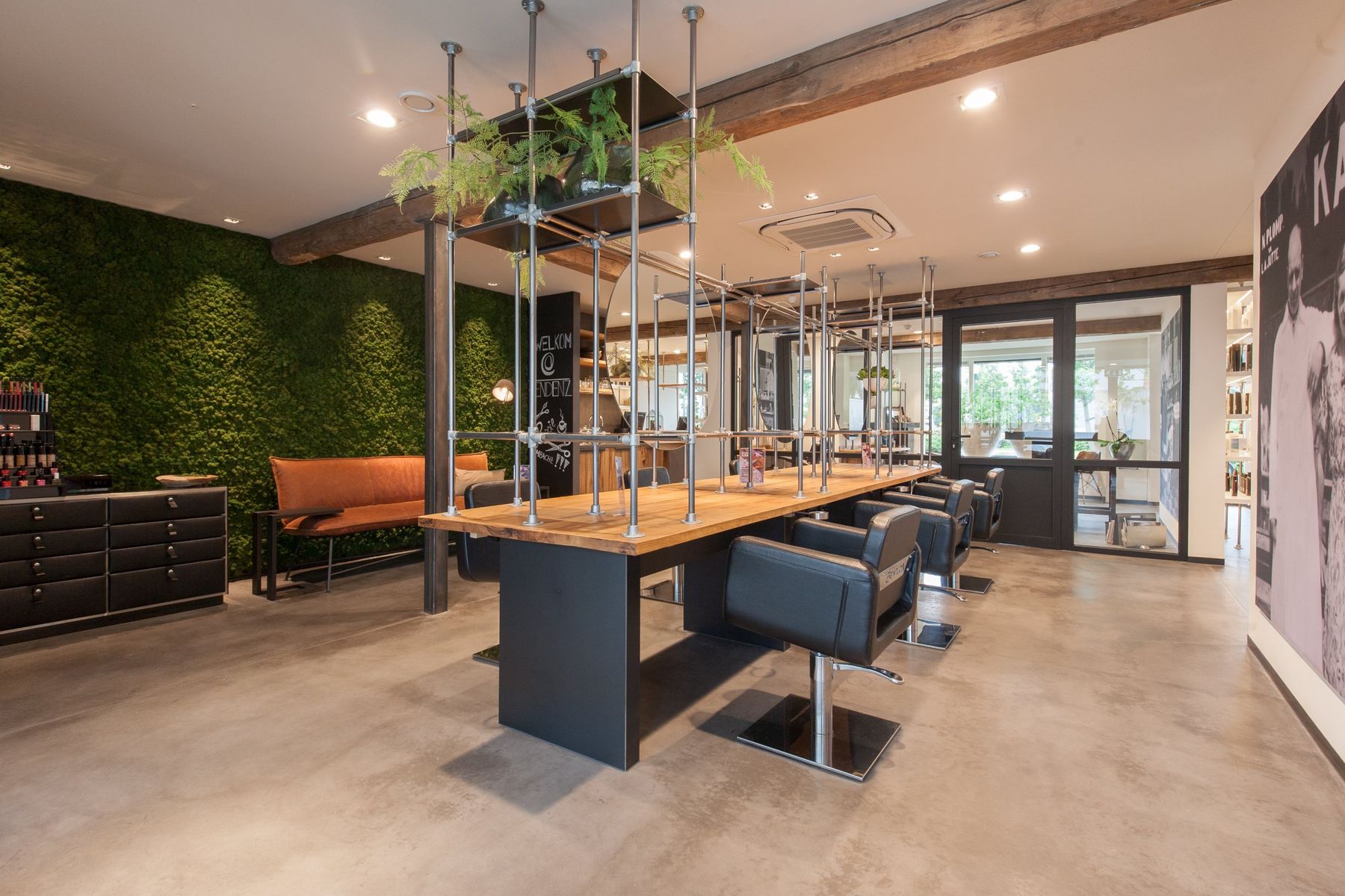 Salon met een lange kappertafel, stalen buizen en een muur van mos